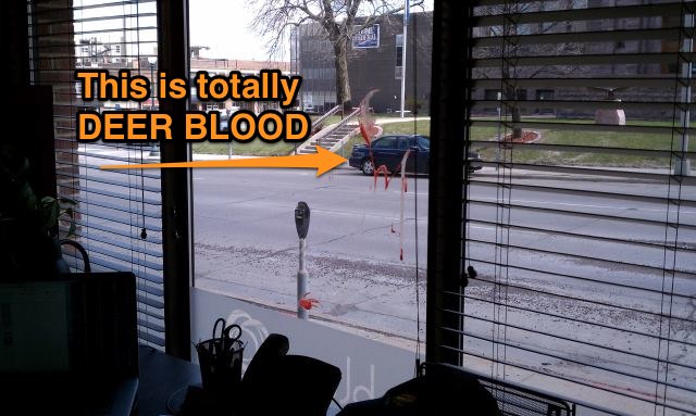 A window with a small amount of deer blood splattered on it, with a label saying "This is totally DEER BLOOD."